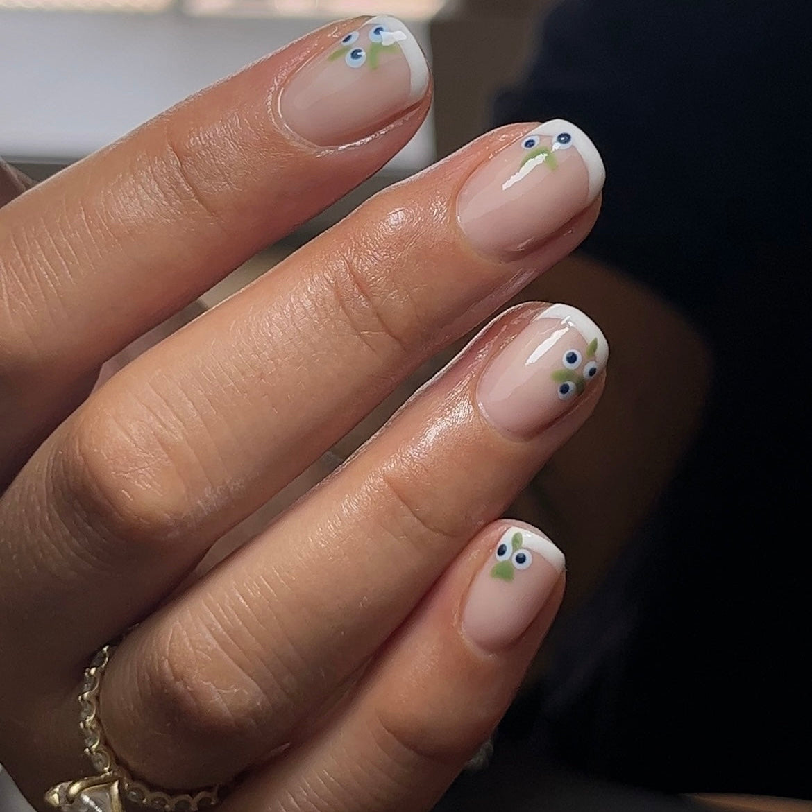 Close-up of a hand with pink nails featuring small decorative elements, wearing a gold ring.