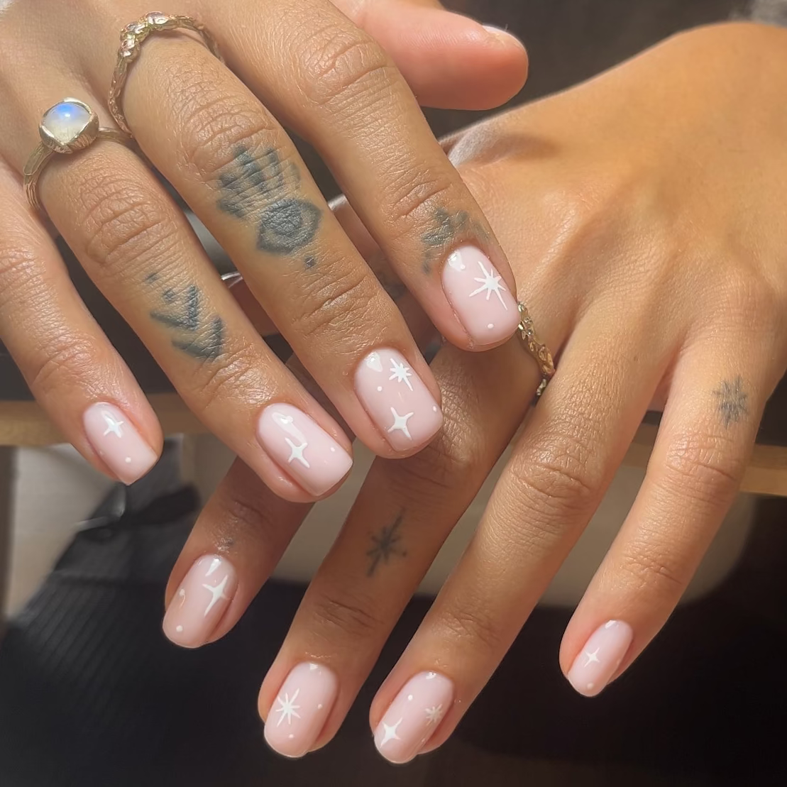 Close-up of hands with tattoos and rings, holding a cup.